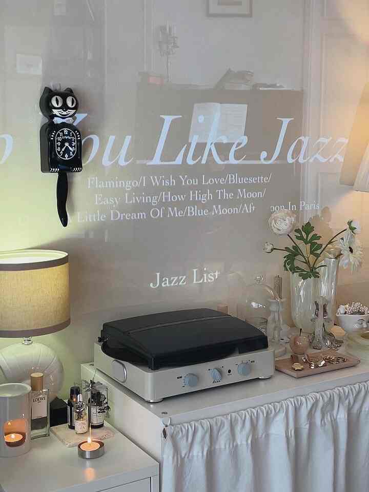 White-toned living room with retro accents featuring a projector screen wall and vintage record player creating a cozy home cafe atmosphere