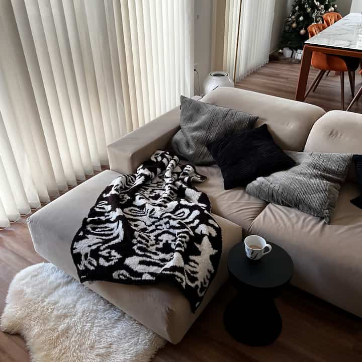 Beige sofa with black cushions and black side table on wood-tone floor in living room space