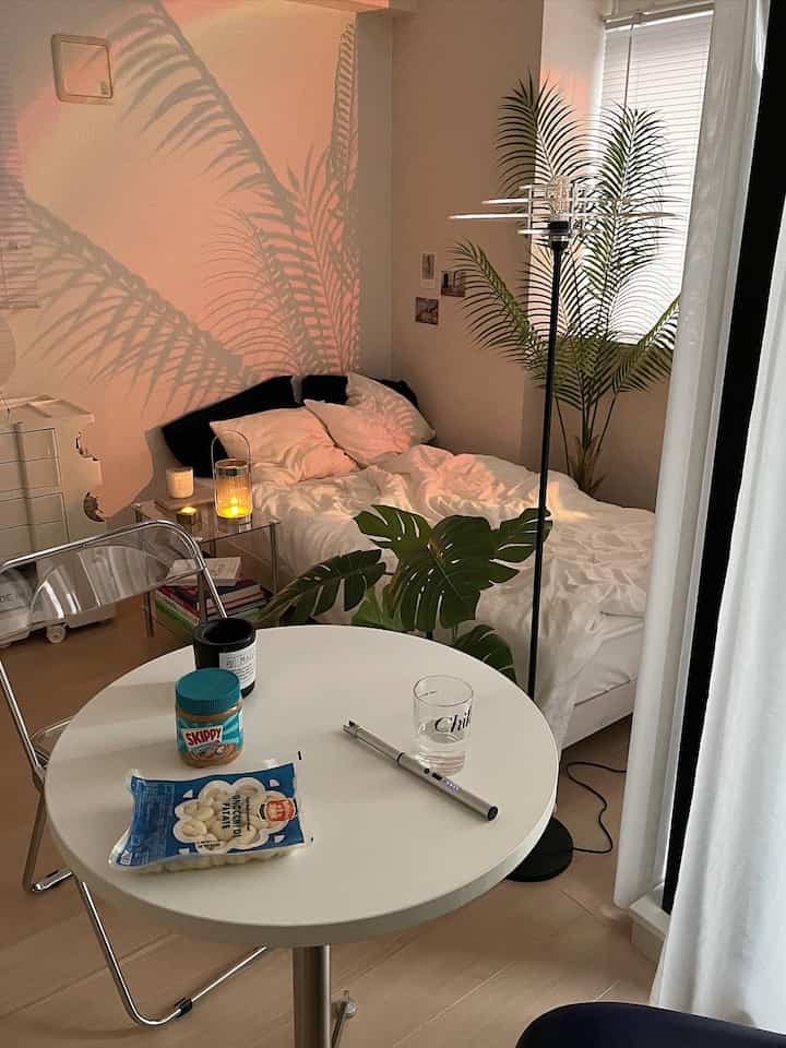 Warm beige and white studio apartment bedroom featuring floor lamp and monstera plant creating a cozy atmosphere