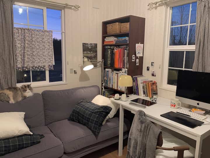 Compact living room in white and gray tones, featuring a sofa, bookshelf, and a cozy small home office setup