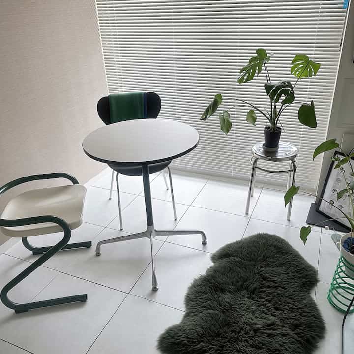 Minimal and natural dining room with white tiled floor and blinds window, featuring plants and stools