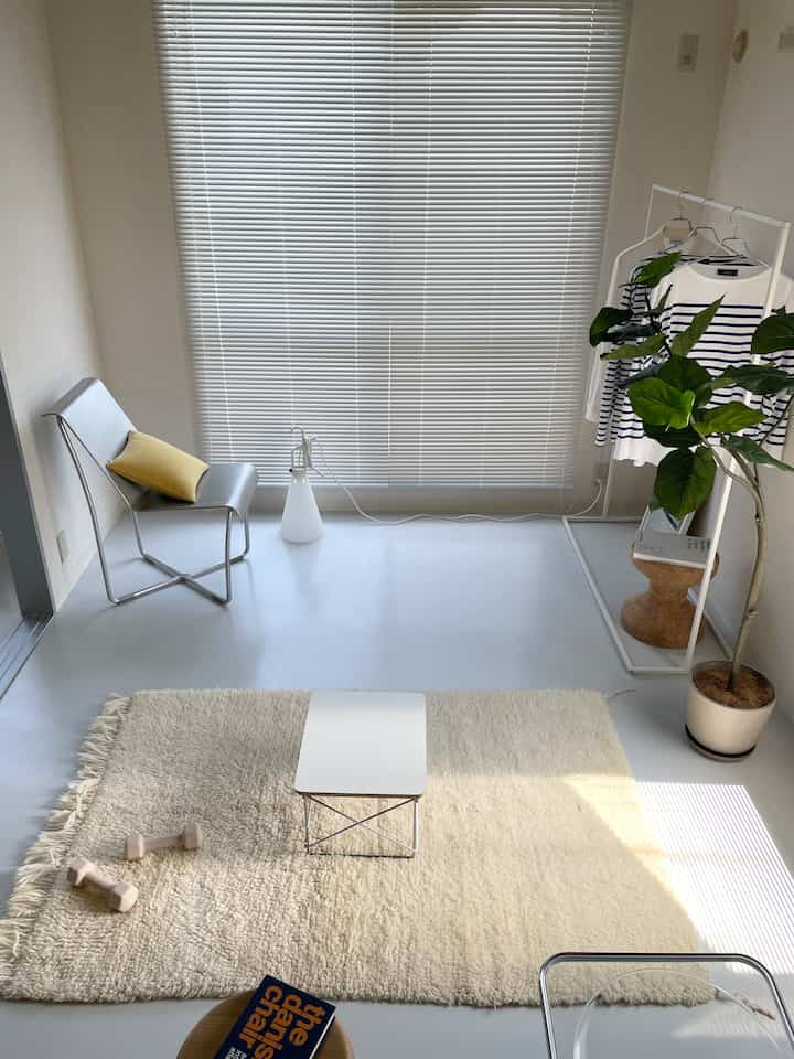 白色を基調としたシンプルなリビング空間、コーナーに配置された白いアイアンハンガーラックとナチュラルなラグが印象的な清潔感のあるインテリア