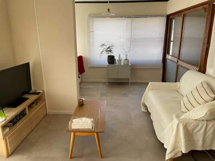 白とベージュの落ち着いた色調のリビング、ソファ、コーヒーテーブル、テレビ台が配置されたミニマルでナチュラルな雰囲気のインテリア