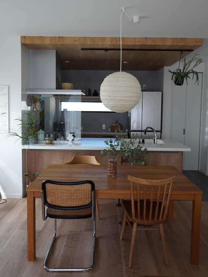 ナチュラルな木目調と白色のキッチンとダイニング、三種類のダイニングチェアが配置された印象的な空間