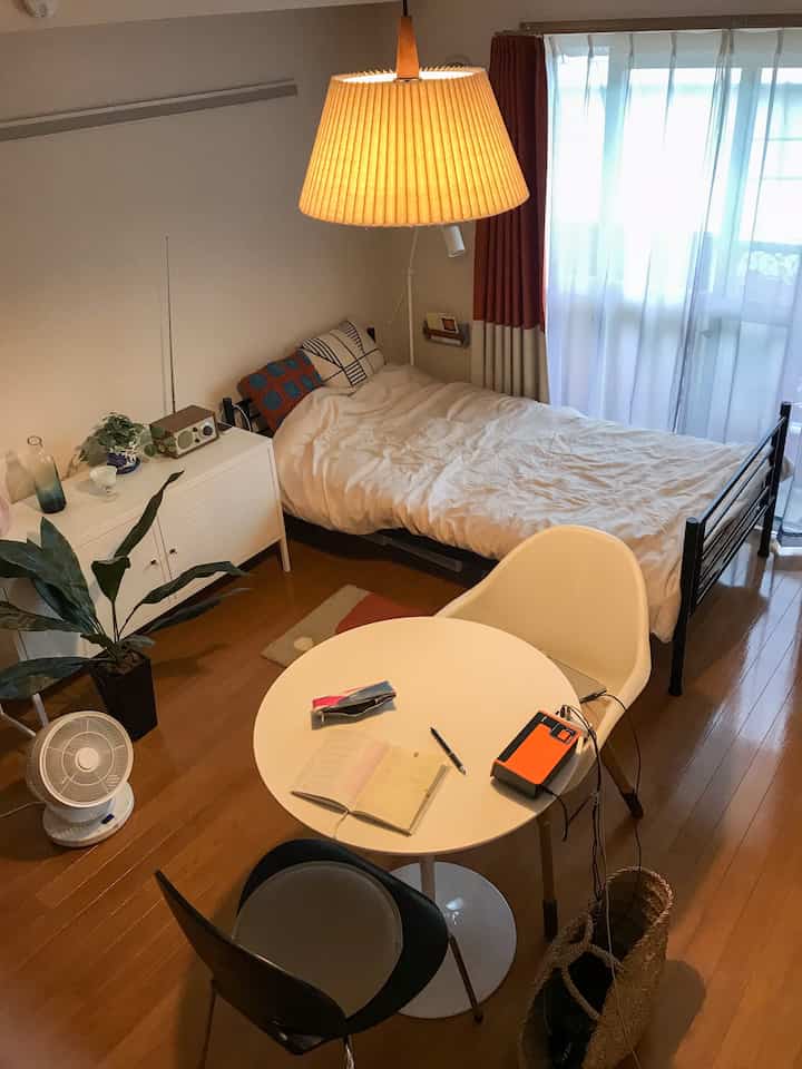 ホワイトとブラウンのトーンが調和するコンパクトな寝室、丸テーブルと収納キャビネットが配置された雰囲気のある空間