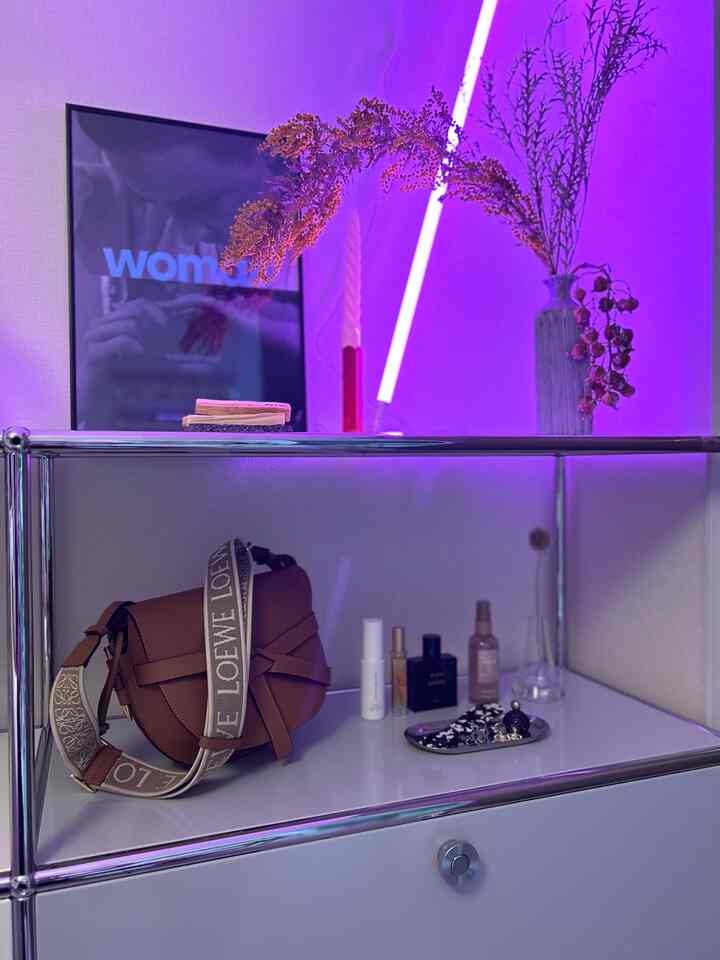 Minimal entrance space featuring a white and silver tone sideboard under purple lighting, decorated with a vase, candle, and a poster
