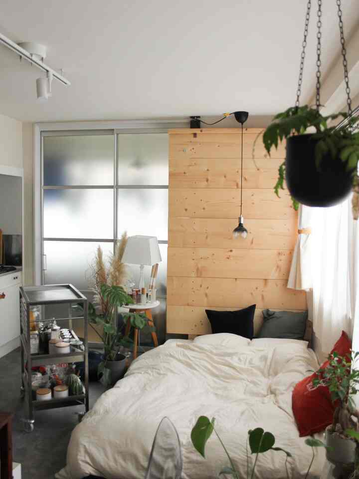 ナチュラルな雰囲気の寝室、木製ヘッドボードと白い寝具、ステンレスのキッチンワゴンと複数の植物が配置された居心地の良い空間