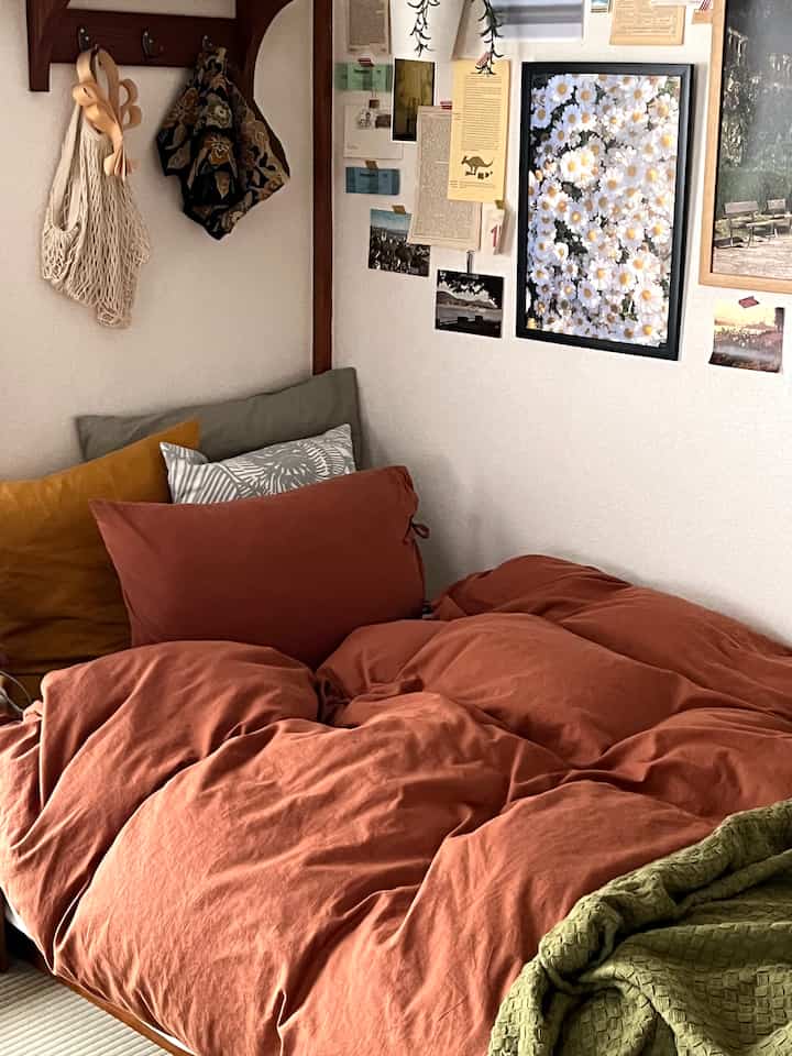 Warm natural color toned bedroom featuring a large rust orange blanket and assorted cushions for a cozy atmosphere