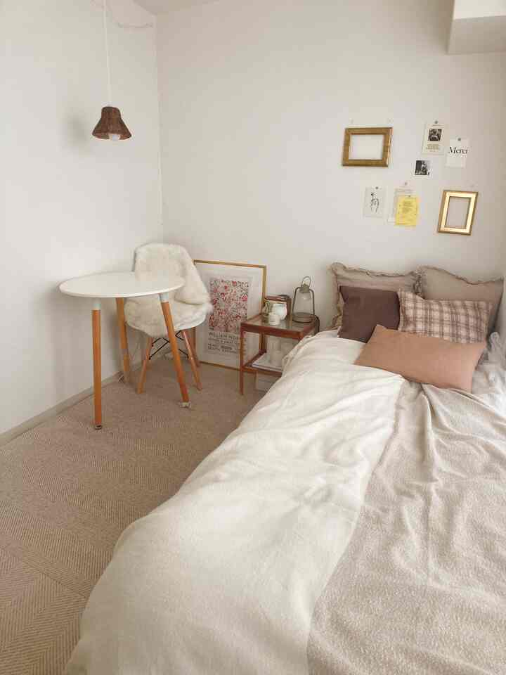 ナチュラルな色調の寝室、白いベッドとナイトテーブル、木の脚のテーブルが配置された雰囲気のある空間