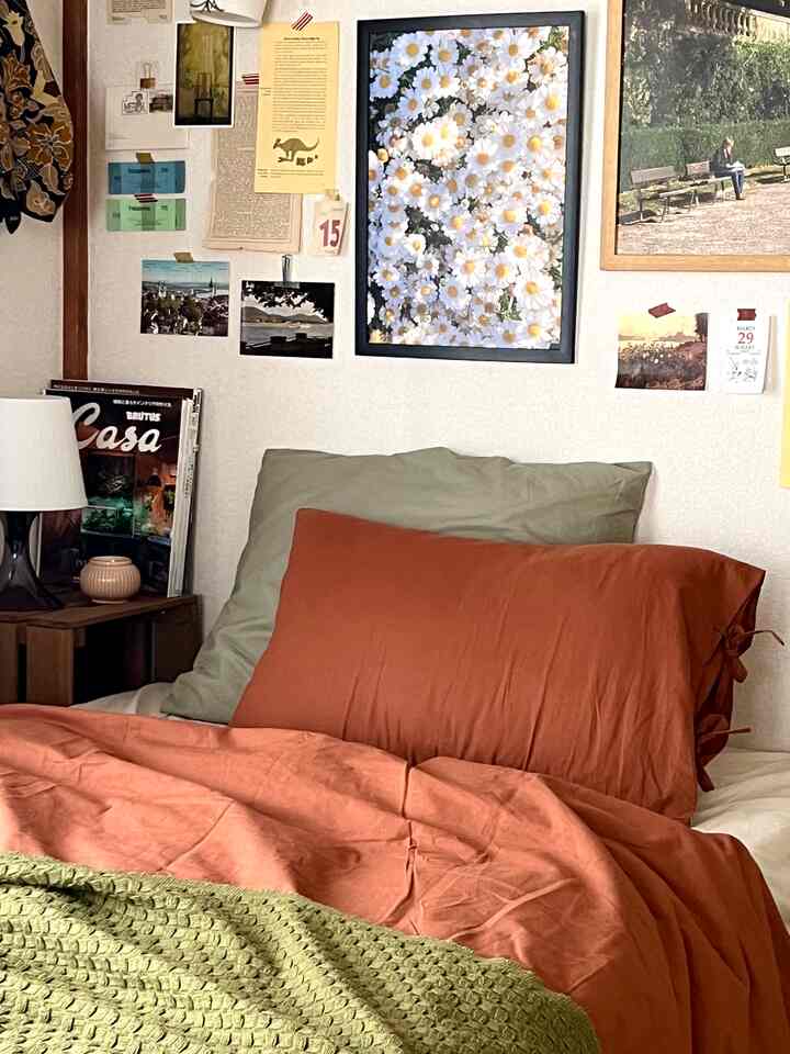 A natural-toned bedroom featuring green and rust orange bedding with various framed wall art creating a cozy atmosphere