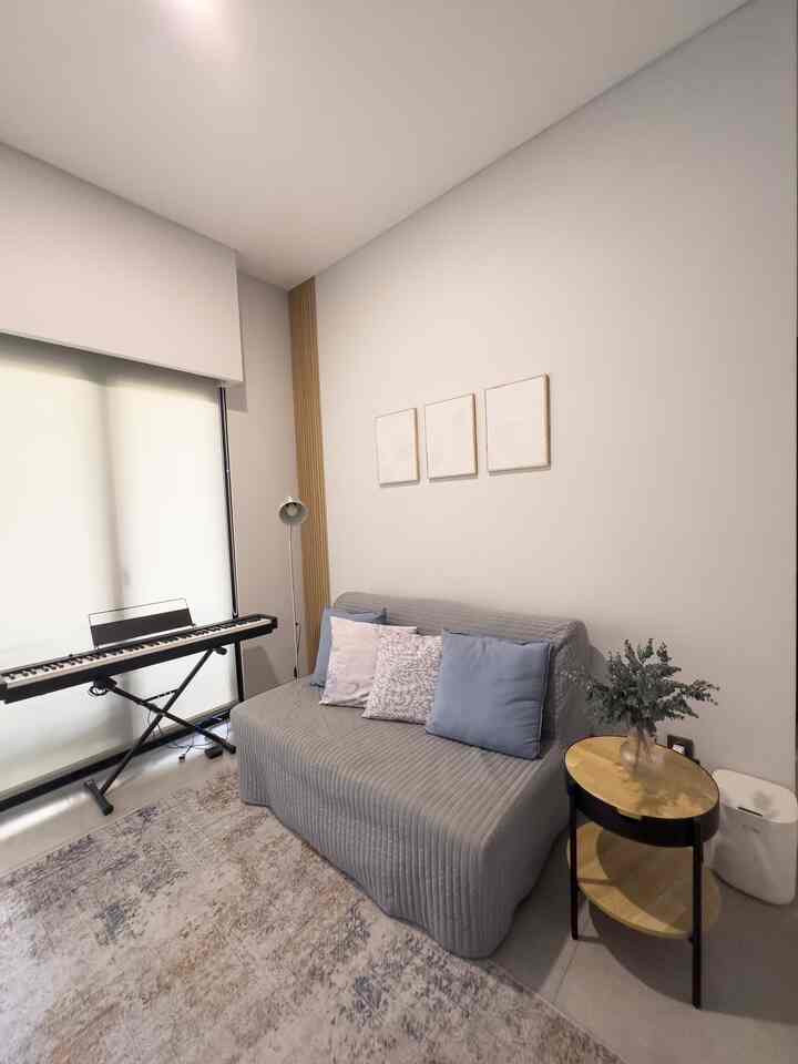 Neutral-toned small living room with wooden accent, featuring a gray sofa and digital piano in a modern, clean design