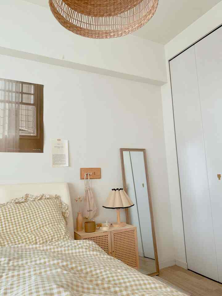 ベージュとホワイトの色調の寝室、チェック柄の寝具と木製のナイトテーブル、全身鏡が配置された雰囲気のあるインテリア