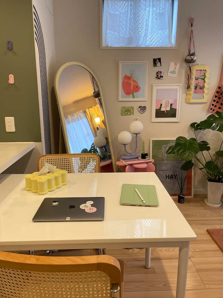 A white and natural-toned living room corner featuring a workspace with laptop and tablet on table, large floor mirror, and a spherical table lamp creating a cozy atmosphere.