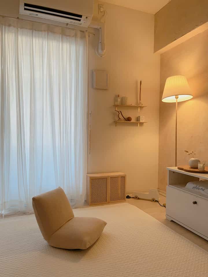 暖かいベージュのナチュラルトーンの小さなリビング、フロアクッションとフロアランプが雰囲気のある空間を演出