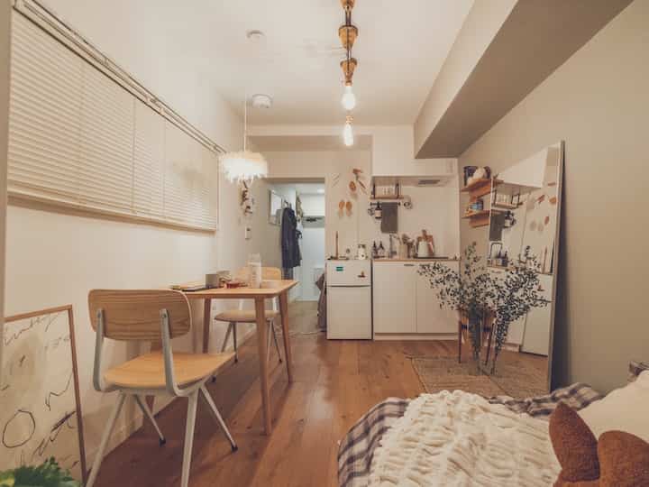 Natural wood tone flooring and white walls define a small studio kitchen and dining space with a cozy, compact atmosphere