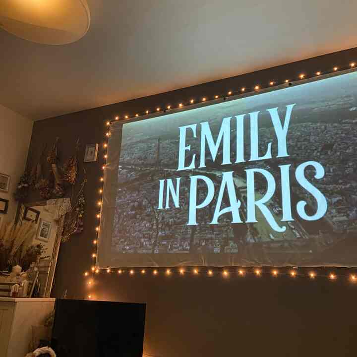 ダークグレーの壁とストリングライトがあるホームシネマ空間、壁に映写機の映像が投影された雰囲気のあるリビング