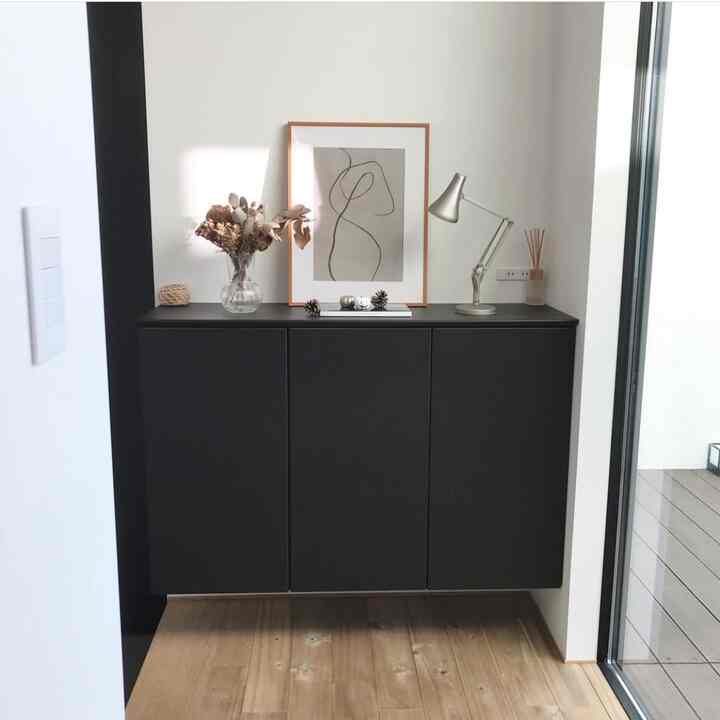 黒のシューズラックが配置されたモダンな玄関、木目調の床とテーブルランプ、花瓶の装飾が調和した印象的なインテリア