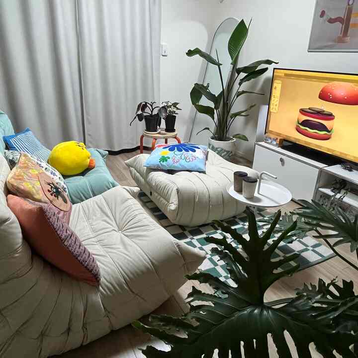 White and green toned 1LDK living room featuring various plants, cozy sofa, and patterned rug creating a warm atmosphere