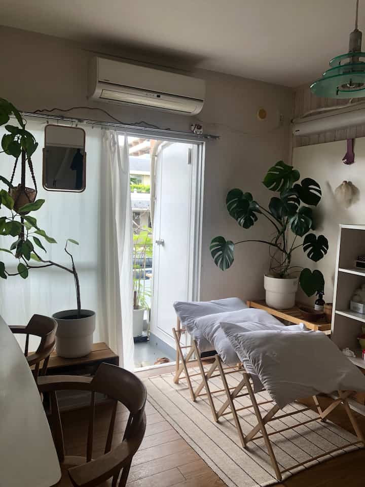 Natural and white toned small room next to veranda featuring wooden furniture and bedspreads laid out on drying racks with a simple atmosphere