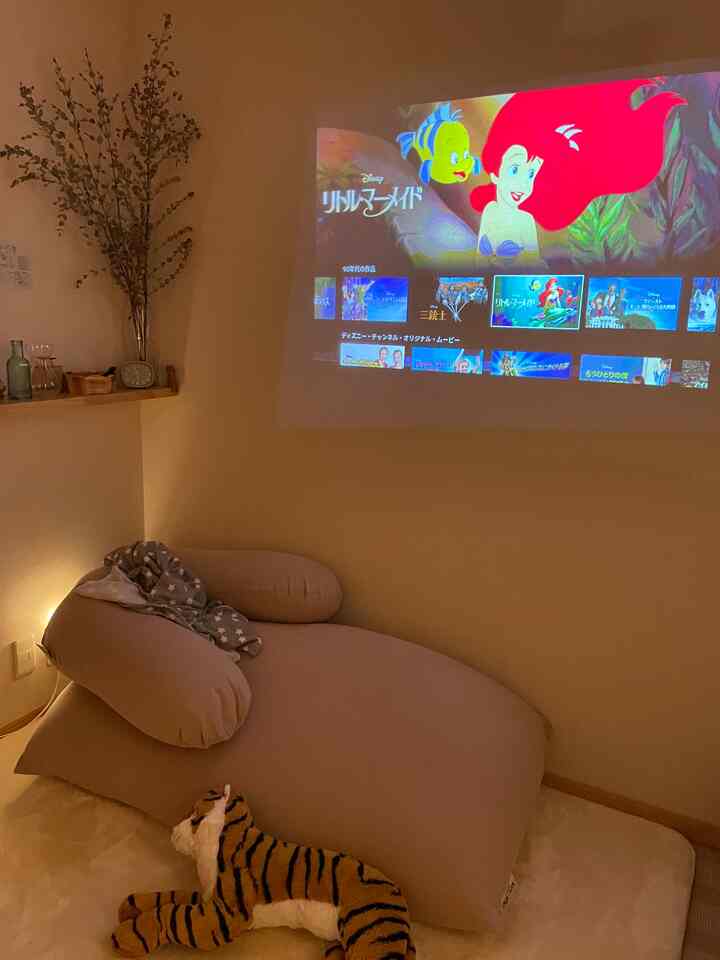 暖かいベージュ色調のリビング、ビーズクッションソファとクッション、壁に映写されるプロジェクター映画が落ち着いたホームシネマの雰囲気を演出