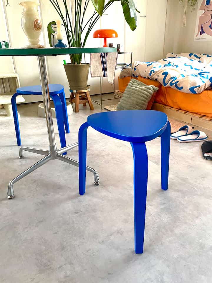 Monotone cement floor studio bedroom featuring vivid blue stools and wooden bed frame
