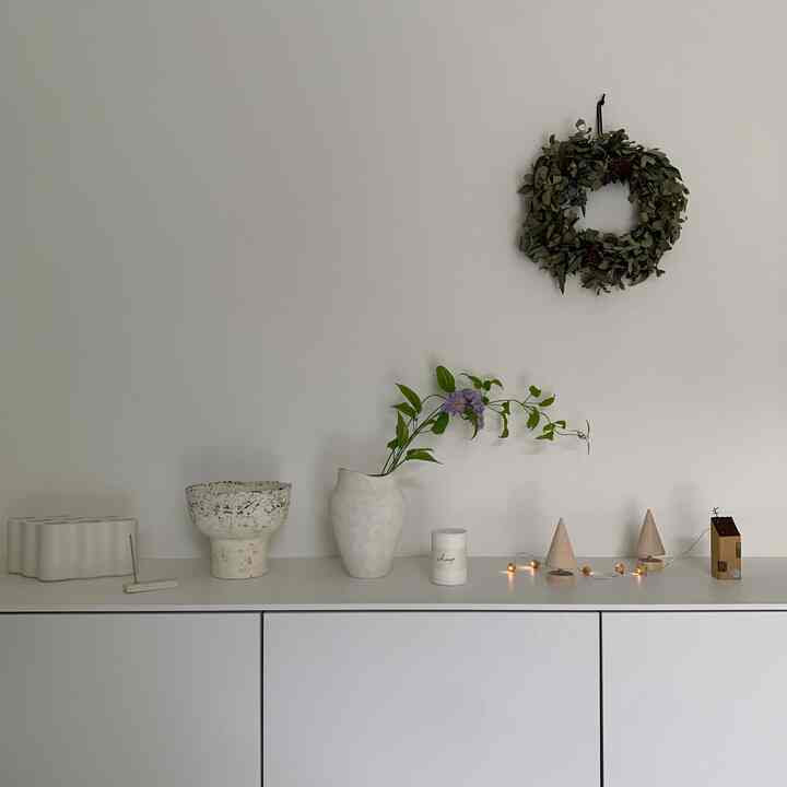 白い壁とキャビネットのあるナチュラルな玄関、花瓶とキャンドル、ガーランドが配された落ち着いた空間