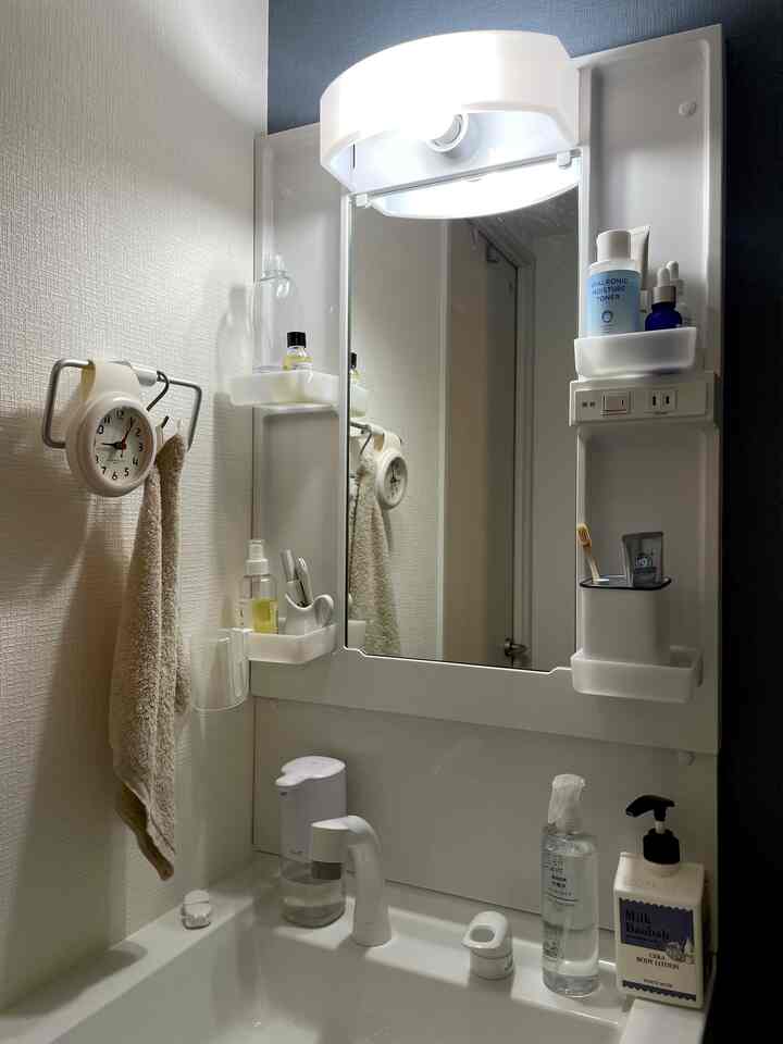 White-toned bathroom featuring sink, mirror, and a wall clock creating a clean and functional space