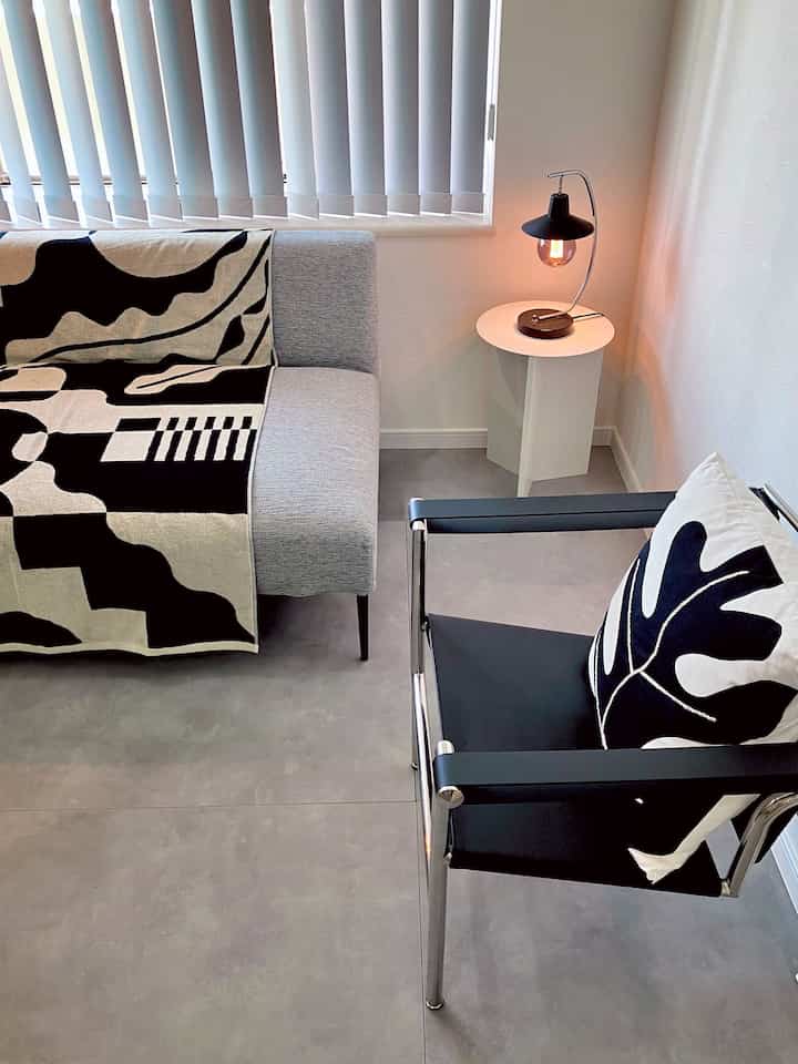 モノトーンのグレー色調のリビング、ミッドセンチュリーモダンスタイルのソファとアームチェア、サイドテーブルが配置されたシンプルで洗練されたインテリア