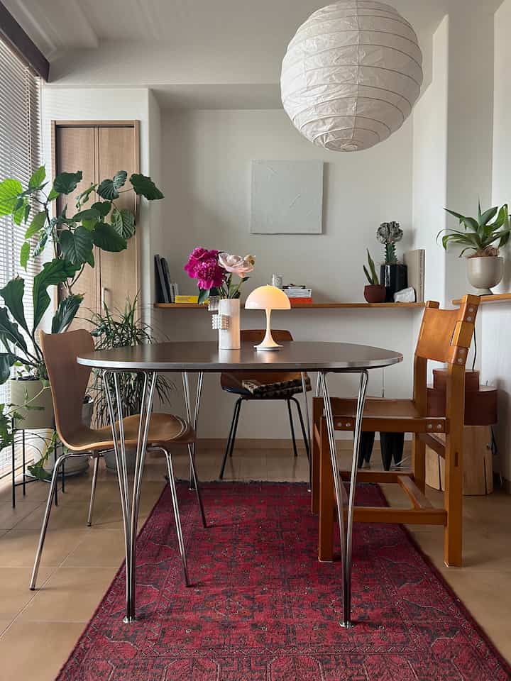 白い壁と木目調家具が調和したダイニング、ヴィンテージのダイニングテーブルと様々な椅子、赤いラグがアクセントの雰囲気あるインテリア