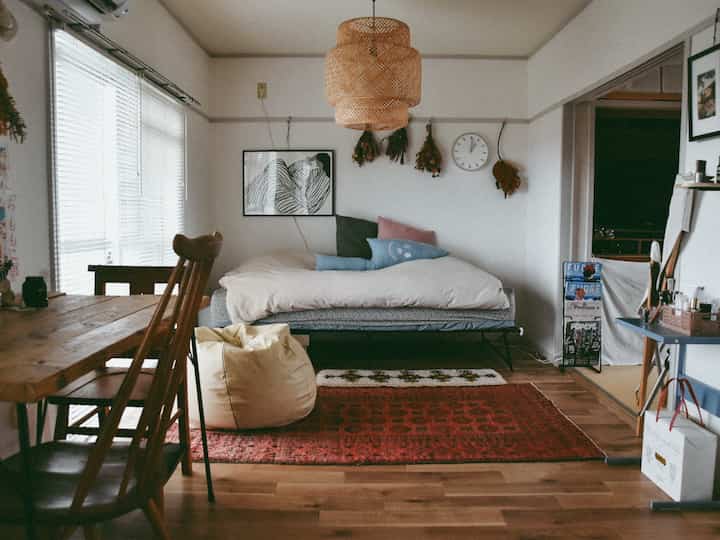 A natural-toned single household bedroom with white walls, brown wooden furniture, and a red rug