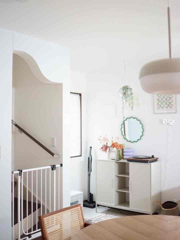 白と木目調の調和が感じられる玄関兼ダイニング空間、丸いダイニングテーブルとサイドボード、植物と時計が配置された印象的なインテリア