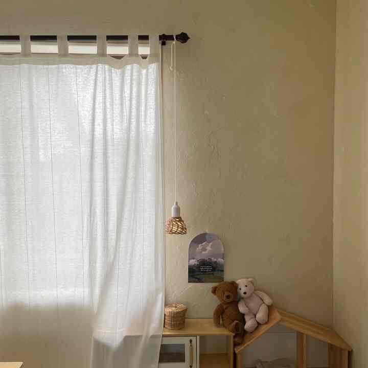 Soft beige kids' room with white cotton curtain and wooden toy house creating a cozy atmosphere
