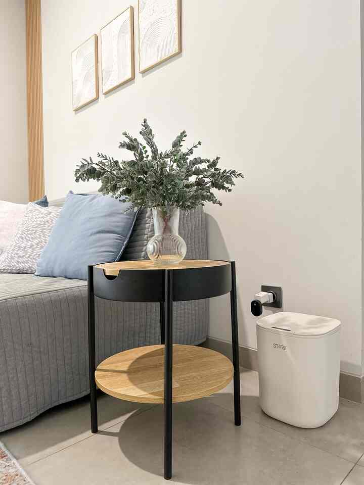 Modern living room featuring gray sofa and wood-toned side table with black legs holding a glass vase of eucalyptus