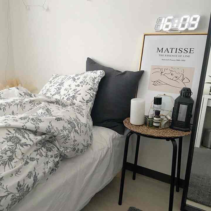 白とグレーのトーンの寝室、花柄の寝具とダークグレーのクッションが配置されたモダンで落ち着いた雰囲気のインテリア