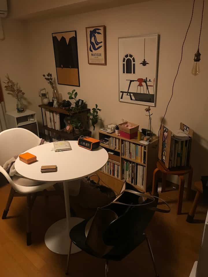 暖かくてナチュラルな色調のダイニング、シンプルな白い丸テーブルと椅子が配置され、ポスターと本棚がある雰囲気のあるインテリア