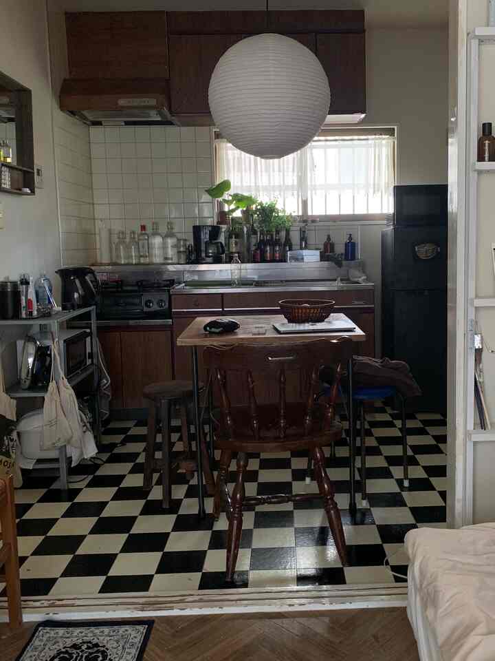 白とダークブラウンのキッチンスペース、チェッカーボードの床と木製のダイニングチェアが配置されたヴィンテージな雰囲気のインテリア