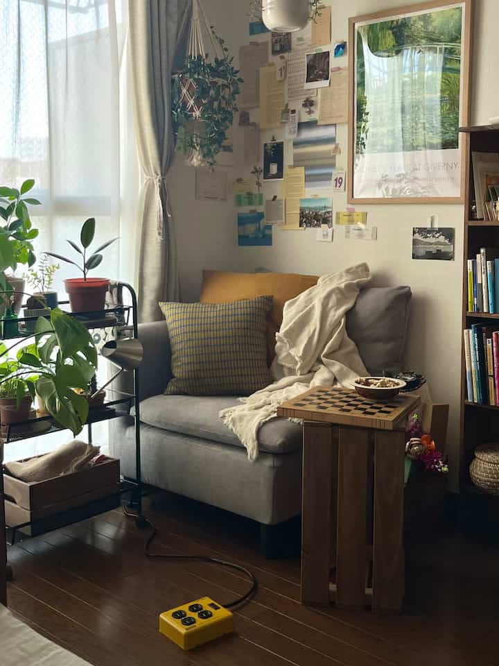 ナチュラルな色調のリビング、グレーのソファと木目調のサイドテーブル、多くの植物が配置された居心地の良い空間