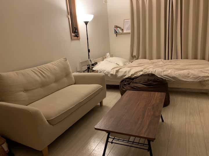 ベージュ色調の小さな寝室、ベージュのソファとベッド、木製のコーヒーテーブルが配置された落ち着いた空間