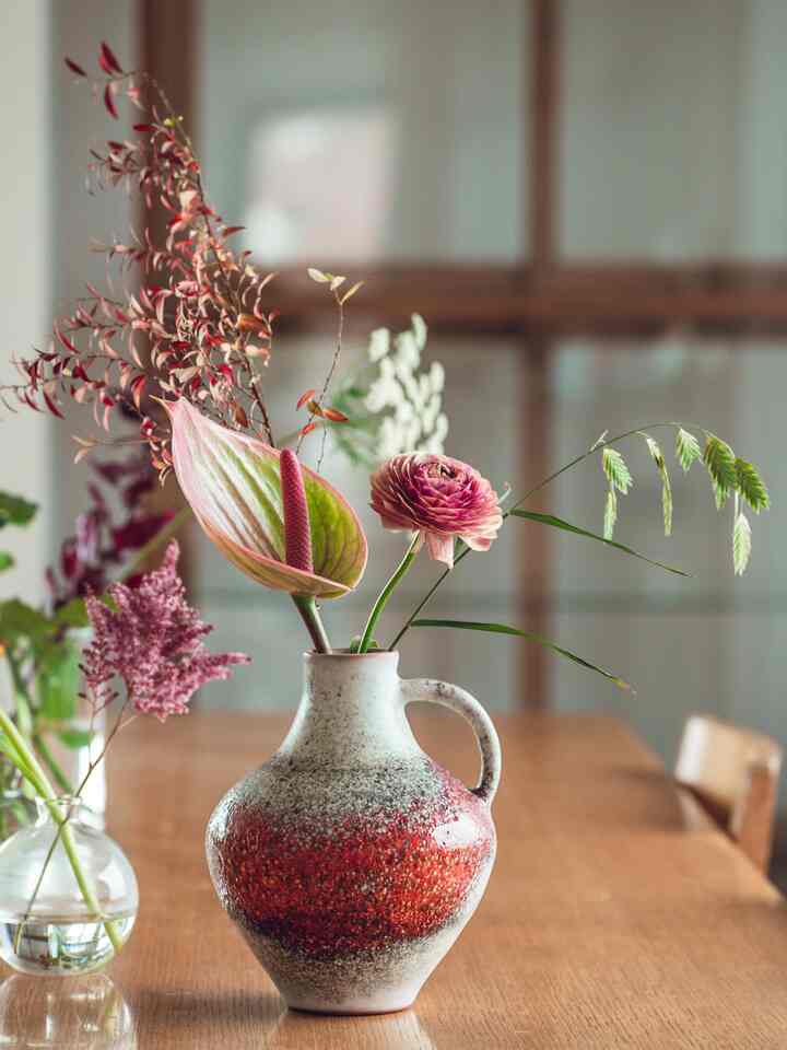 木目調のダイニングテーブルに置かれた赤い模様のセラミック花瓶と様々な花が配置されたナチュラルな印象のダイニング空間