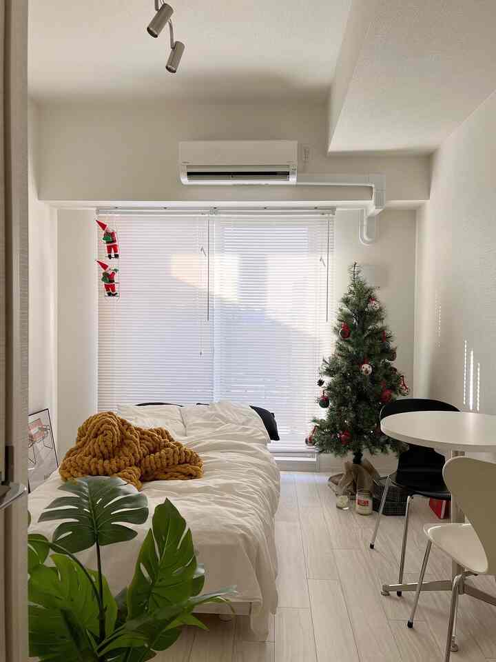 白い壁とブラインドのある一人暮らしの寝室、クリスマスツリーとダイニングテーブルが配置された雰囲気のある空間