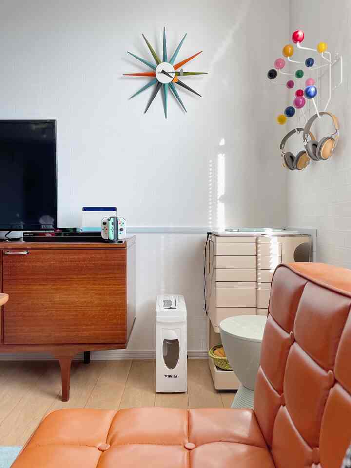 白い壁と茶色の木製家具、オレンジ色のレザーソファが配されたレトロなミッドセンチュリーモダンの印象的な空間