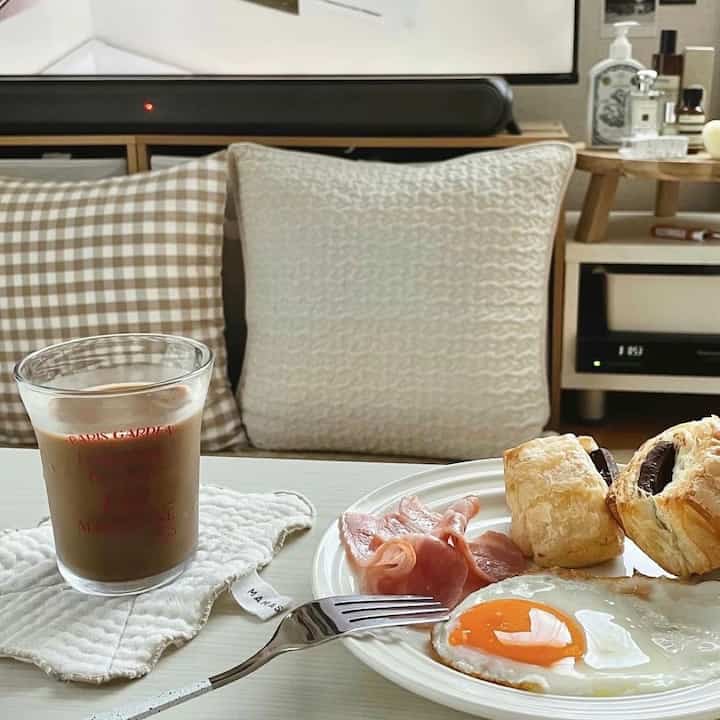 Beige and white toned living room space featuring cushions on a sofa and a coffee table with a prepared breakfast creating a cozy atmosphere