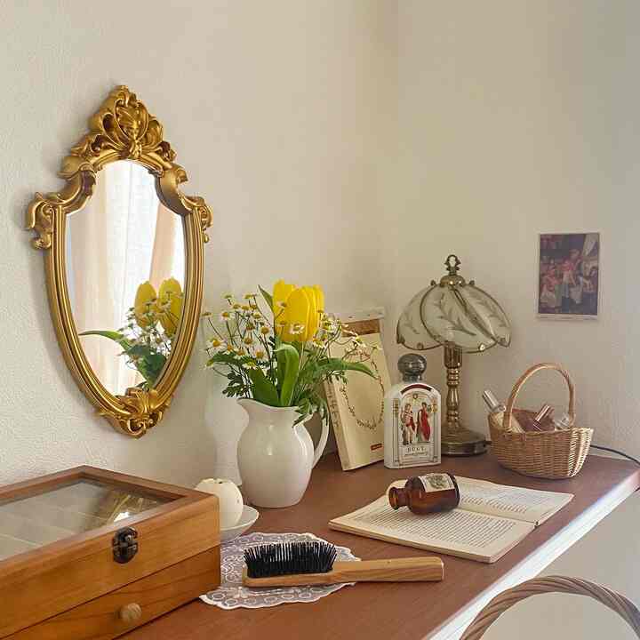 Natural-toned walk-in closet with white walls, featuring a gold decorative mirror and floral vase on a cozy vanity table