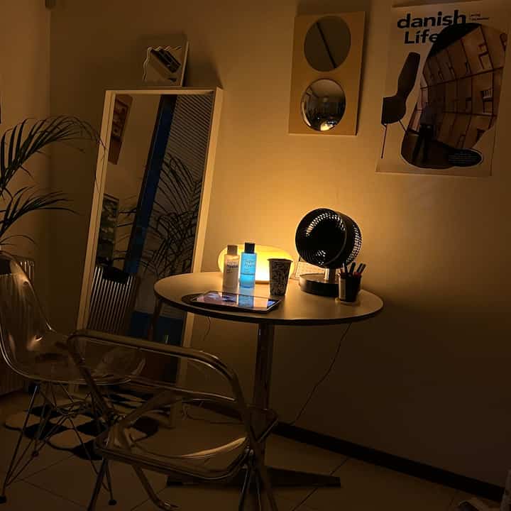 Warmly lit white studio apartment with transparent chairs and round table, mirrors and posters on walls in a modern setting