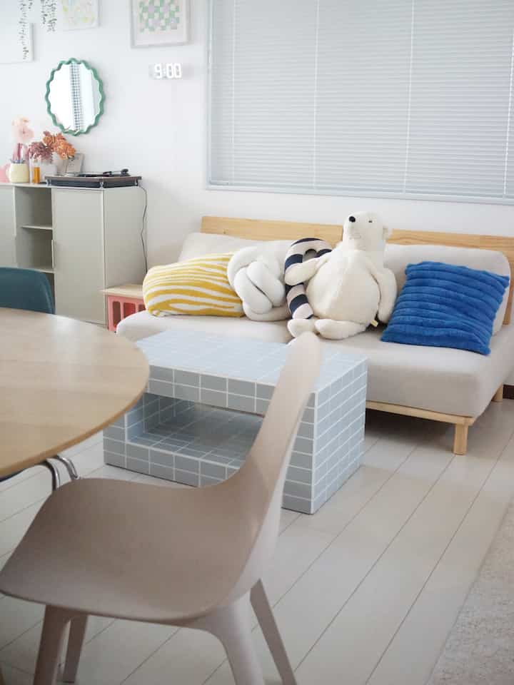 白とベージュの色調のリビング、ベージュのソファに青いクッション、タイル模様のコーヒーテーブルが配置されたシンプルでモダンな印象の空間