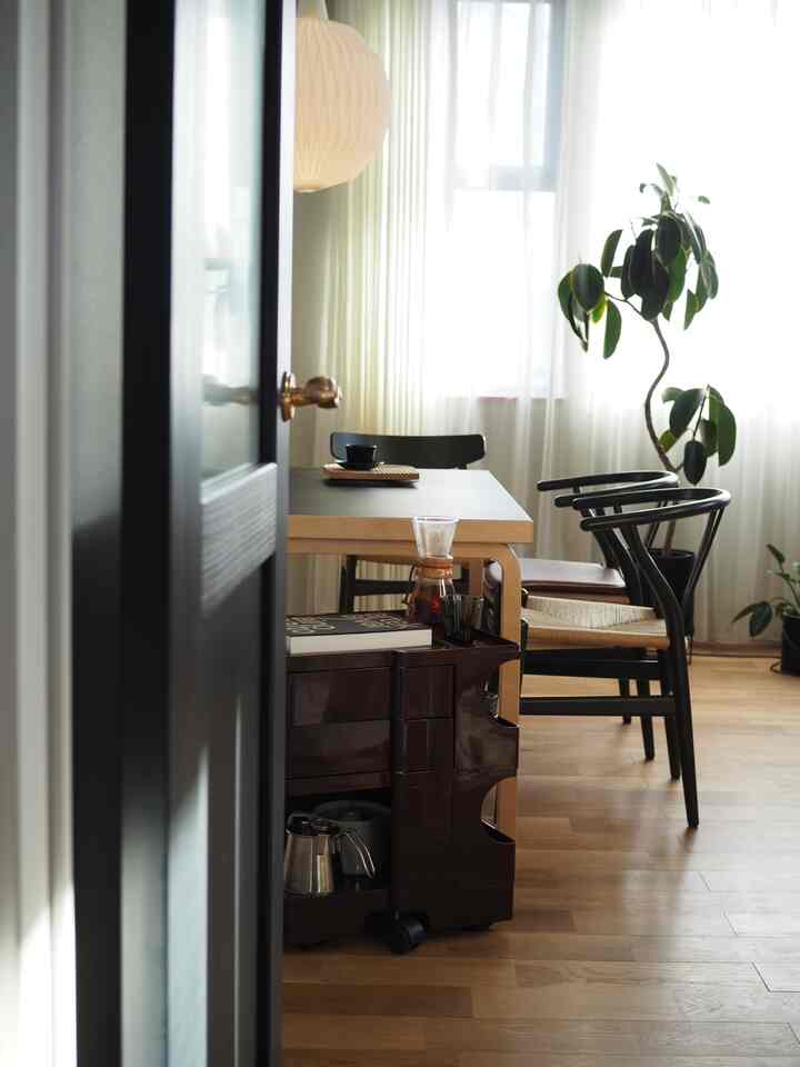 Dining room with natural light and brown wood tones, featuring a boby wagon and wishbone chairs in a calm setting
