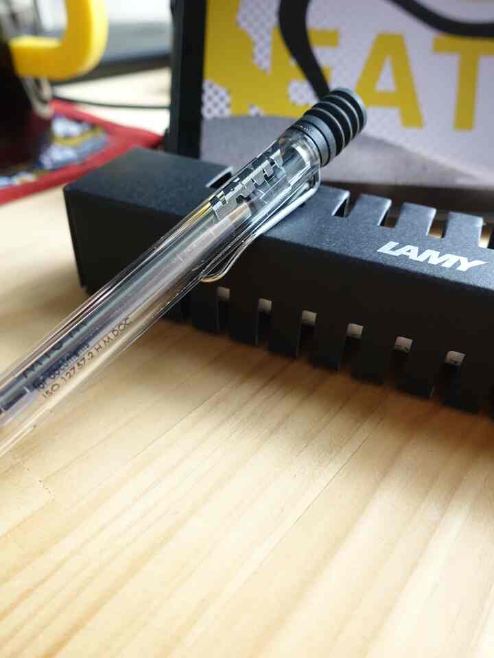 明るい木目調のデスクに黒いLAMYのペンとロゴ入りのペンケースが置かれた清潔感のある作業空間