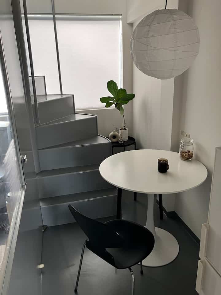 グレーとホワイトのトーンでまとめられた狭いモダンな一人暮らしのダイニング、丸テーブルと黒い椅子が配置された空間