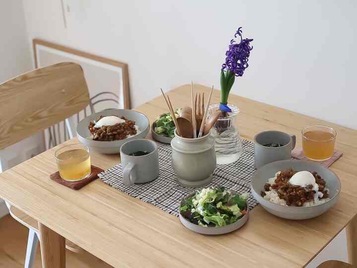 ナチュラルなトーンのキッチンダイニングテーブル、二人分の食器と料理がシンプルに配置された雰囲気のあるインテリア