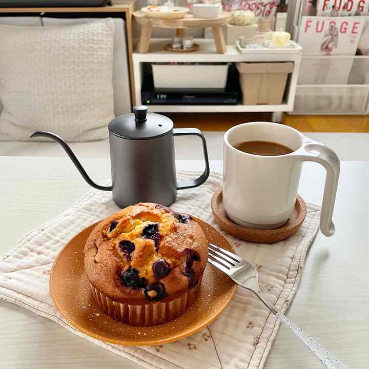 白と茶色のトーンのあるおうちカフェ、コーヒーマグとドリップポットが置かれたダイニングテーブルの上にブルーベリーマフィンとキッチンタオルが配された雰囲気のあるインテリア